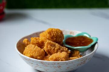 Fried chicken with chicken dipping sauce in a ceramic cup on a white table.