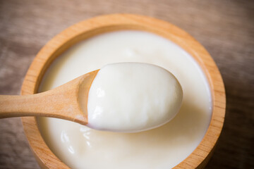 White yogurt in a wooden cup with a wooden spoon