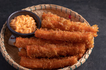 Crab sticks battered and breadcrumbs fried with mayonnaise sauce in white cups on a black table