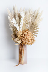 Dried flower arrangement in a pink vase. Including Banksia, Hydrangea, pampas grass, Palm Fronds, cream Ruscus leaves, and rust Amaranthus. Photographed on a white background.