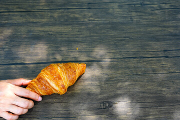Woman's hand holding the croissant on wooden background.