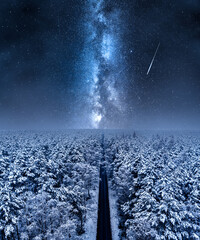 Milky way over long road and snowy forest.