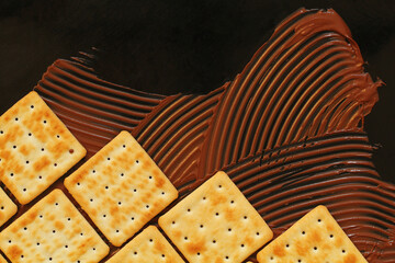 crackers and chocolate paste on black background, cookies lined up like brickwork, copy space for...