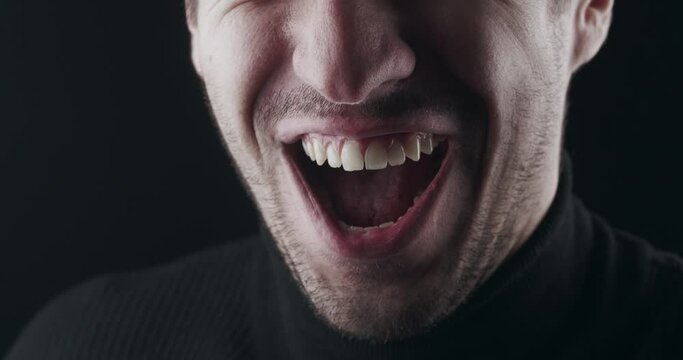 Close-up of angry laugh. Macro shot of mouth of a mad angry man smiling ominously on black background