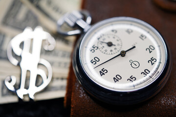 Dollar close-up. Money macro shot. The stopwatch lies on paper banknotes and a leather wallet. Clock, watch, timepiece, timer, clock face, mechanical device, speedometer                            