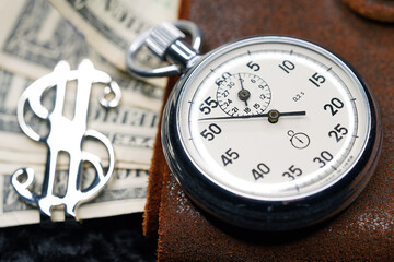 Fototapeta premium Dollar close-up. Money macro shot. The stopwatch lies on paper banknotes and a leather wallet. Clock, watch, timepiece, timer, clock face, mechanical device, speedometer 