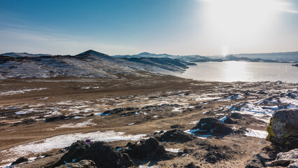 The frozen lake is surrounded by mountains. Snow covered earth. Sun glare on ice. There are no people. Clear blue sky, winter day. Baikal