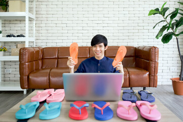 Fototapeta premium Young asian man sells various styles of rubber slippers online via application on laptop computer. Small home business concept.