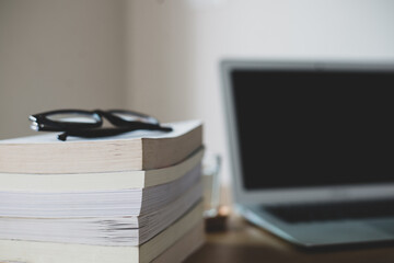 Eyeglasses, book, laptop place on old wooden office desk.