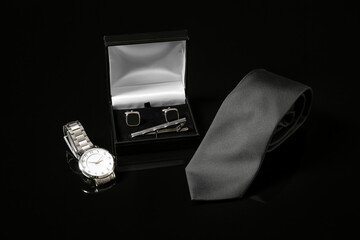 Wristwatch with cufflinks and necktie on dark background