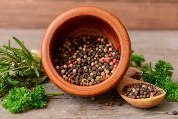 Bowl and spoon with peppercorns on wooden background