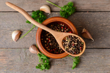 Bowl and spoon with peppercorns on wooden background