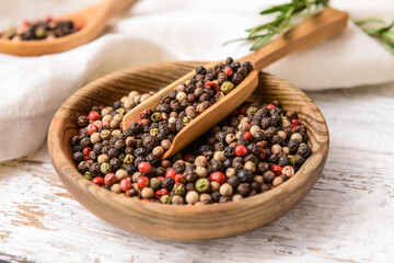Bowl and scoop with peppercorns on light wooden background