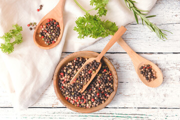 Bowl and scoop with peppercorns on light wooden background