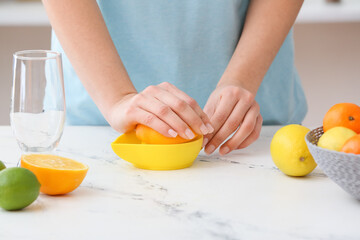 Woman squeezing orange on table in kitchen