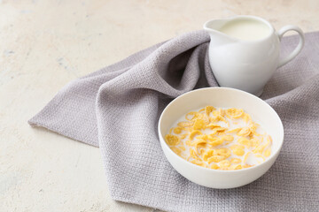 Bowl with tasty cornflakes and jug of milk on light background