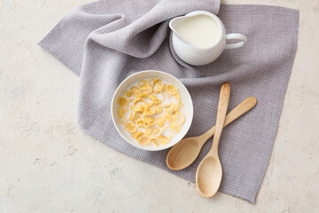 Bowl with tasty cornflakes and jug of milk on light background