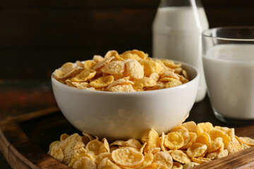 Glass of milk and bowl with tasty cornflakes on grunge background