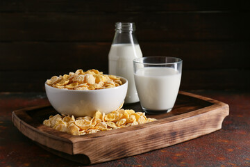 Glass of milk and bowl with tasty cornflakes on grunge background