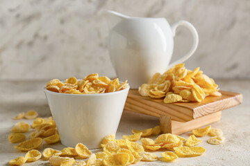 Bowl with tasty cornflakes and jug of milk on light background