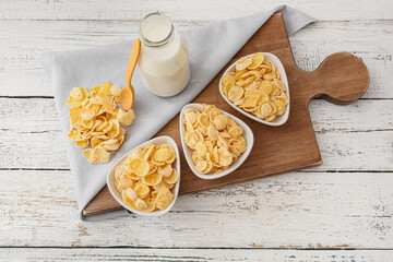 Fototapeta na wymiar Bowls with tasty cornflakes and bottle of milk on light wooden background