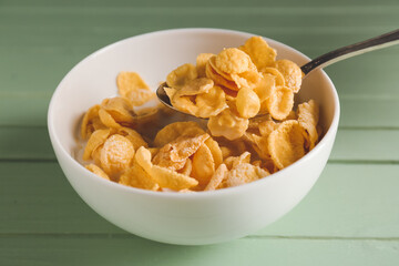 Bowl and spoon of tasty cornflakes with milk on color wooden background