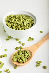 Bowl and spoon with green coffee beans on light background