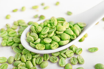 Spoon with green coffee beans on light background, closeup