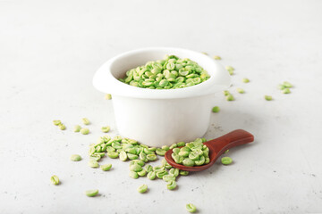 Bowl and spoon with green coffee beans on light background