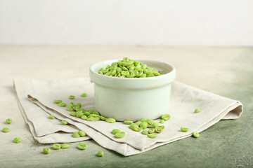 Bowl with green coffee beans on color background