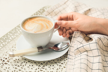 Female hand with cup of hot cappuccino on light background