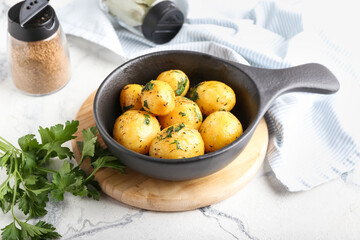 Frying pan of tasty potatoes with parsley on light background