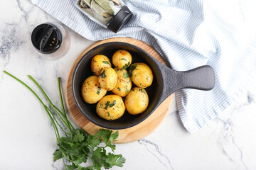 Frying pan of tasty potatoes with parsley on light background