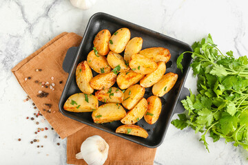Baking sheet of tasty potatoes with parsley on light background