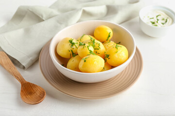 Bowl of tasty boiled potatoes with parsley on light background