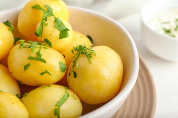 Bowl of tasty boiled potatoes with parsley on light background