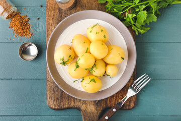 Plate of tasty boiled potatoes with parsley on color wooden background