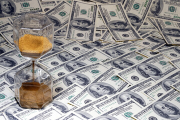 Time is money. Hourglass stand on a layer of notes. Dollars. Watch. Clock. Countdown. American currency. Dollars                                