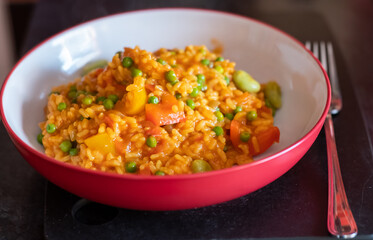 Close up of a healthy, nutritious and homemade vegetable paella in a red dinner bowl with selective focus, shallow depth of field and bokeh