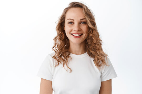 Smiling blond woman with white perfect smile and natural face, looking happy and confident at camera, standing in t-shirt against white background