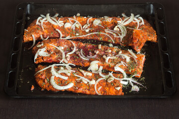 Baking tray with strips of Iberian ribs, with strips of onion, garlic and herb sauce, and wine ready to cook.