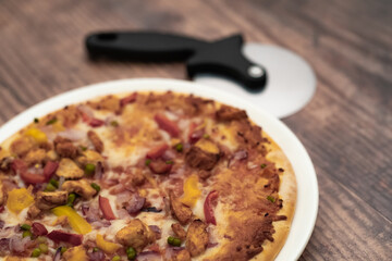 Close up and selective focus of a home cooked thin crust sweet chilli chicken pizza on a white plate on a wooden table