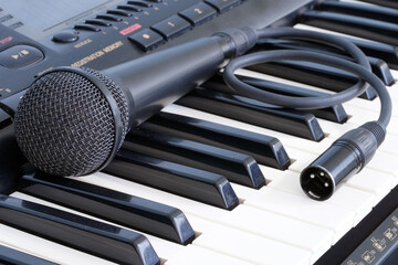 The black microphone lies on the keyboard of the synthesizer. Musical instruments. Karaoke and vocals. Art.                               