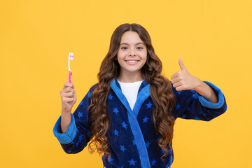 cheerful teen girl with curly hair in comfortable pajama presenting toothbrush, thumb up