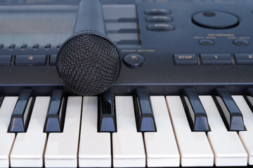 The black microphone lies on the keyboard of the synthesizer. Musical instruments. Karaoke and vocals. Art.                               