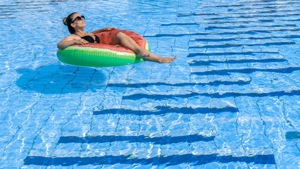 Swimming pool holidays. Happy young sexy girl in bikini swimsuit, sunglasses and inflatable rubber ring swimming in blue water. Summer luxury vacation in spa resort pool.