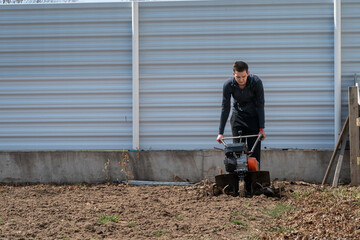 A young man digs the ground in the garden with a motorcultivator