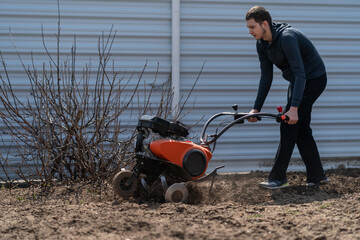 A young man digs the ground in the garden with a motorcultivator