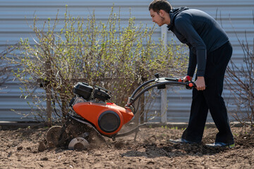 Fototapeta na wymiar A young man digs the ground in the garden with a motorcultivator