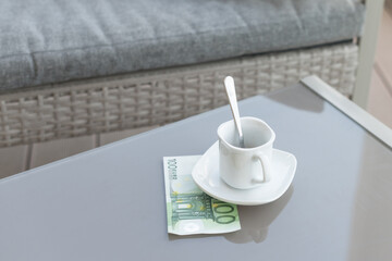 One hundred euro and empty cup of coffee on a glass table of outdoor cafe. Payment, tip.